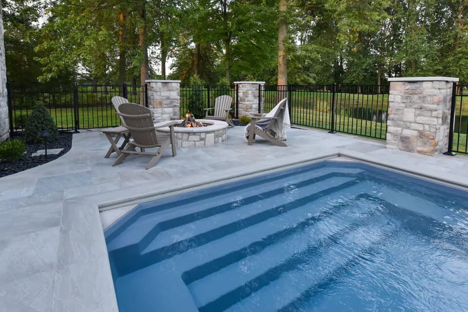 Pool and spa steps with paver deck, stone piers, firepit seating, and fence line